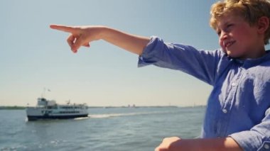 Portrait of a Happy Smiling Boy with Curly Hairs Travelling on Board of a Small Sightseeing Ship. He Points to Something with His Arm