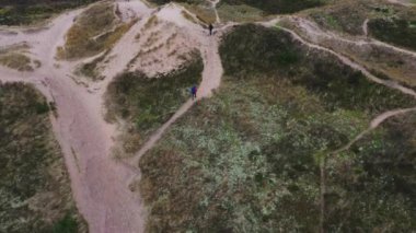Aerial Of Tourists Hiking Along the Grass Covered Sand Dunes with Many Trails. High Angle Shot