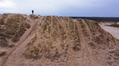 Aerial Side View Wide Shot Of a Tourist Standing on a Top of a Sand Dune and Enjoying the View. Camera Zooms Out