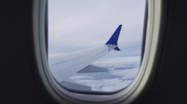View Through Plane Window on an Aircrafts Wing and Passing By Clouds During the Flight. Beautiful Scenery Outside the Window