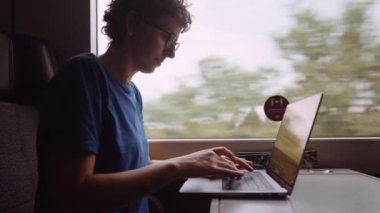 Woman with Curly Hairs and with Glasses On Working on a Laptop While Going by Train. Slow Motion Shot