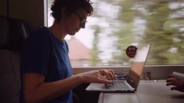 Woman with Curly Hairs and with Glasses On Working on a Laptop While Going by Train. Slow Motion Shot