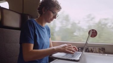 Woman with Curly Hairs and with Glasses On Working on a Laptop While Going by Train. Slow Motion Shot