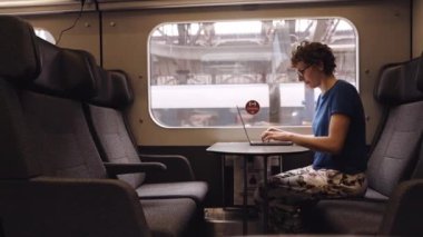 Woman with Curly Hairs and with Glasses On Working on a Laptop While Waiting for the Train Departure. Panning Shot