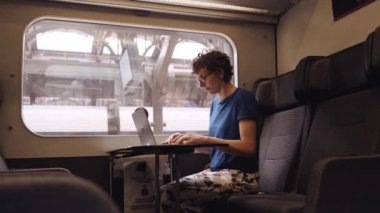 Woman with Curly Hairs and with Glasses On Working on a Laptop While Waiting for the Train Departure. Camera Is on the Opposite Seat