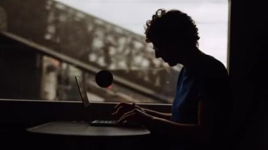 Silhouette of a Woman with Curly Hairs and with Glasses On Working on a Laptop While Going by Train. She Is Sitting at the Table by the Window