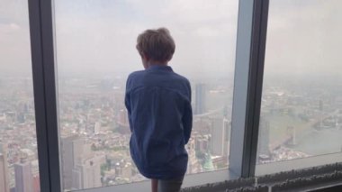 Medium Slow Motion Handheld Arcing Shot Of Young Boy Looking Through Skyscraper Window To New York City Below