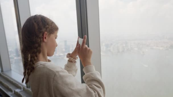 Medium Slow Motion Handheld Shot Girl Filming Smartphone Window Skyscraper — Vídeo de Stock