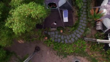 Aerial View of a Luxury Resort Tent House Between Coconut Trees in Tropical Forest. Pretty Woman Is on the Terrace in Front of the Tent. Top Down Zoom Out Shot