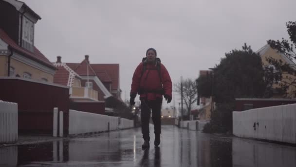 Man Backpack Walking Wet Asphalt Road Reflections Surface Residential Houses — 图库视频影像