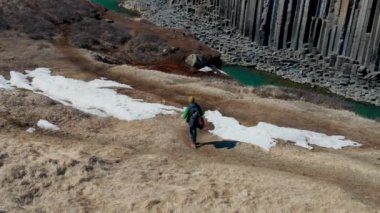 Wide Drone Flight Tracking Man With Backpack Hiking Over Terrain By The  Studlagil Canyon, Glacier Valley, Jokuldalur, Iceland