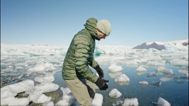 Человек Турист Садится Снимает Одну Перчатку Касается Воды Ледниковой Лагуны — стоковое видео