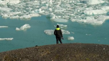 Man Photographer with Camera in His Hand Goes Down the Hill in Front of Jokulsarlon Glacier Lagoon, Iceland. Slow Motion Shot