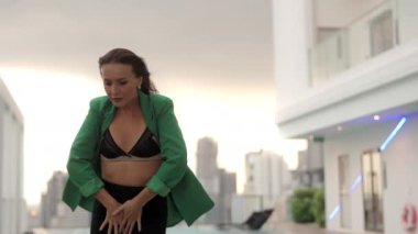 Medium Slow Motion Handheld Tracking Shot Of Sensuous Dancer Posing To Camera In Bra And Green Jacket At Poolside