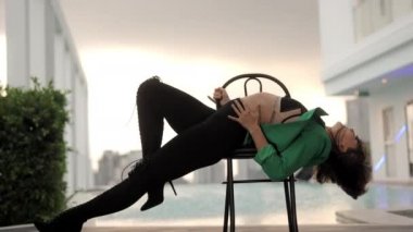 Dolly Slow Motion Wide Shot Of Young Sensuous Dancer Leaning Back On Chair In High Heels And Bra At Poolside