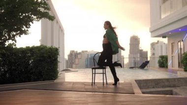 Lockdown Wide Slow Motion Shot Of Dancer Posing And Turning On Chair In Green Jacket In High Heels At Poolside
