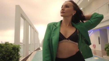 Medium To Wide Slow Motion Dolly Shot Of Young Dancer With Hand In Windswept Hair Standing In High Heels And Bra And Posing With Chair At Poolside