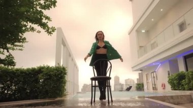 Wide Slow Motion Dolly Shot Pulling Back From Dancer In High Heels And Bra Posing With Chair At Poolside