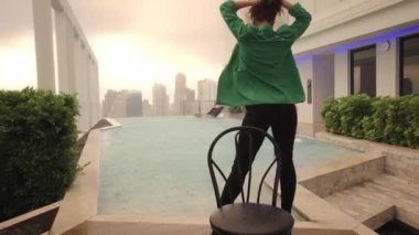 Wide Dolly Slow Motion Shot Of Young Dancer Posing Next To Chair In Bra And High Heels At Poolside
