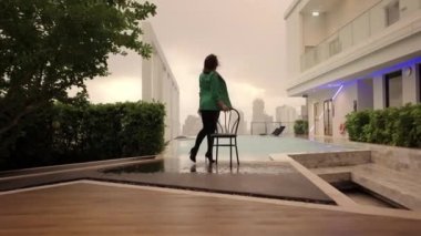 Slow Motion Wide To Medium Dolly Shot Of Dancer Posing By Chair And Crouching At Poolside