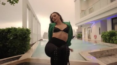 Wide To Medium Slow Motion Dolly Shot Of Sensuous Dancer In Bra And Heels Sitting And Posing On Chair To Camera At Poolside