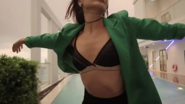 Tracking Medium Slow Motion Shot Of Sensuous Dancer In Bra And Jacket At Poolside Looking To Camera