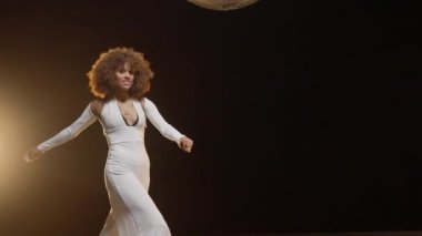 Charming African American Woman with Fluffy Afro Style Hairs in White Jumpsuit Wearing Roller Skates Rides Around on the Stage. Cinematic Slow Motion Shot