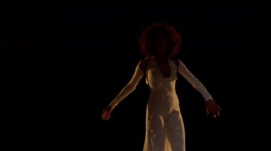 Charming African American Woman with Fluffy Afro Style Hairs in White Jumpsuit Wearing Roller Skates Rides on the Stage. She Moves Towards Camera. Cinematic Slow Motion Shot