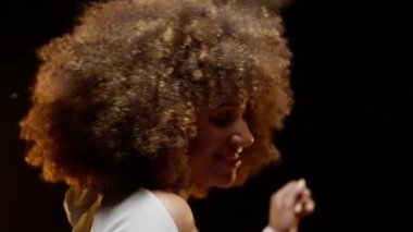 Portrait of Smiling African American Woman with Afro Style Hairs in White Jumpsuit Dancing on the Stage Under Shiny Disco Ball. Cinematic Slow Motion Shot. Camera Follows the Woman