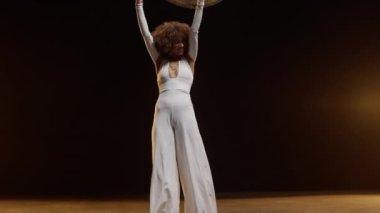 Smiling African American Woman with Afro Style Hairs in White Jumpsuit Wearing Roller Scates Dancing on the Stage Under Shiny Disco Ball. Cinematic Slow Motion Zoom In Shot