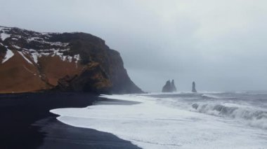 Wide Drone Flight Pulling Back Over Misty Coastline And Black Sand Beach From Sea Stacks In Spring, Iceland