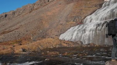 Wide Panning Slow Motion Shot Of Photographer With Camera And Backpack Standing On Rocks And Looking Up At Dynjandi Waterfall, Arnarfjordur, Westfjords, Iceland