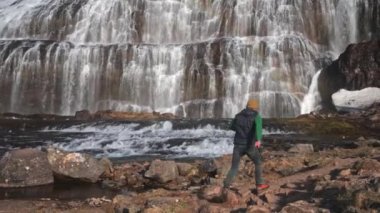 Wide Tracking Slow Motion Shot Of Man Stepping Over Rocks In Front Of Dynjandi Waterfall, Arnarfjordur, Westfjords, Iceland