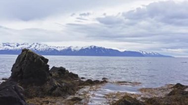 Aerial of Magnificent  Seascape of North Iceland Shore. Snow Capped Mountains and Arch Rock Near Town of Husavik. Drone Flies Backwards Through the Arch