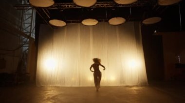 Silhouette of a Professional Dancer Performing in Studio in Soft Warm Lighting. Graceful Young Woman in White Clothes with Long Blond Hairs Dancing in Flashing Lights. Slow Motion Shot
