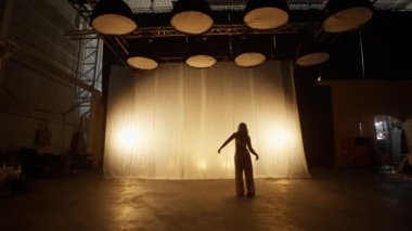 Silhouette of a Professional Dancer Performing in Studio in Soft Warm Lighting. Graceful Young Woman in White Clothes with Long Blond Hairs Dancing in Flashing Lights. Slow Motion Shot
