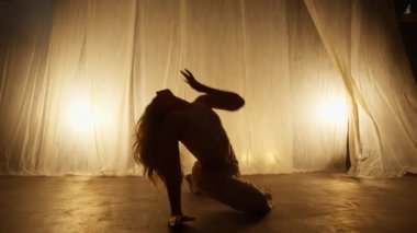 Silhouette of a Professional Dancer Performing in Studio in Soft Warm Lighting. Graceful Young Woman with Long Blond Hairs Dancing in Flashing Lights. Slow Motion Dolly Out and In Shot