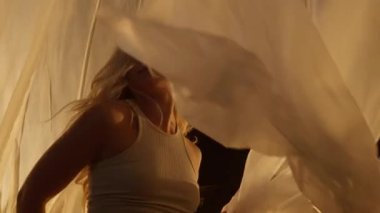 Close-up of a Professional Dancer Performing in Studio in Soft Warm Lighting. Graceful Young Woman with Long Hairs Dancing with White Stage Curtain. Slow Motion Shot