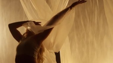 Professional Dancer Performing in Studio in Soft Warm Lighting. Graceful Young Woman with Long Hairs Dancing with White Stage Curtain. Slow Motion Dolly Out Shot