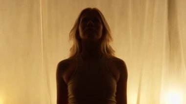 Portrait of a Professional Dancer in Soft Warm Lighting. Graceful Young Woman in White Clothes with Long Hairs Stands in Flashing Lights Against Stage Curtain. Slow Motion Zoom In Shot