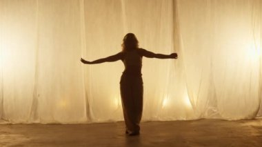 Silhouette of a Professional Dancer Performing in Studio in Soft Warm Lighting. Graceful Young Woman in White Clothes with Long Blond Hairs Dancing in Flashing Lights. Slow Motion Shot