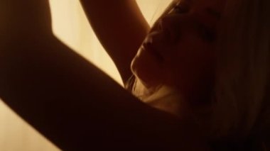 Portrait of a Professional Dancer in Soft Warm Lighting. Graceful Young Woman in White Clothes with Long Hairs Dancing in Flashing Lights Against Stage Curtain. Slow Motion Close-up Shot