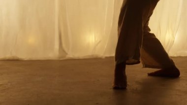 Close-up of a Professional Dancers Legs Performing on the Studios Stage in Soft Warm Lighting. Graceful Young Womans Legs in White Pants. Slow Motion Shot