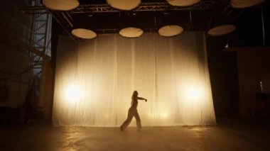 Silhouette of a Professional Dancer Performing in Studio in Soft Warm Lighting. Graceful Young Woman in White Clothes with Long Blond Hairs Dancing in Flashing Lights. Slow Motion Shot