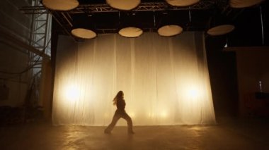 Silhouette of a Professional Dancer Performing in Studio in Soft Warm Lighting. Graceful Young Woman in White Clothes with Long Blond Hairs Dancing in Flashing Lights. Slow Motion Shot