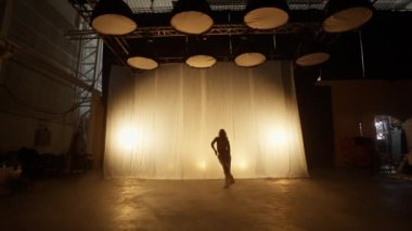 Silhouette of a Professional Dancer Performing in Studio in Soft Warm Lighting. Graceful Young Woman in White Clothes with Long Blond Hairs Dancing in Flashing Lights. Slow Motion Shot