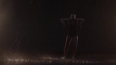Sensual Young Woman Dancer Performing in the Rain in Dark Studio Against Black Backdrop and with Some Spotlights On. Water Drops Falling on the Floor Imitating Rain Shower