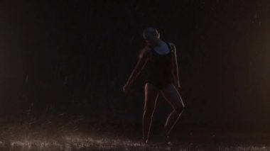 Sensual Young Woman Dancer Performing in the Rain in Dark Studio Against Black Backdrop and with Some Spotlights On. Water Drops Falling on the Floor Imitating Rain Shower