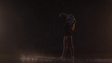 Sensual Young Woman Dancer Performing in the Rain in Dark Studio Against Black Backdrop and with Some Spotlights On. Water Drops Falling on the Floor Imitating Rain Shower
