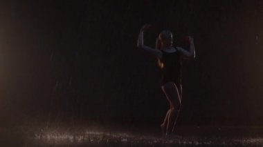 Sensual Young Woman Dancer Performing in the Rain in Dark Studio Against Black Backdrop and with Some Spotlights On. Water Drops Falling on the Floor Imitating Rain Shower